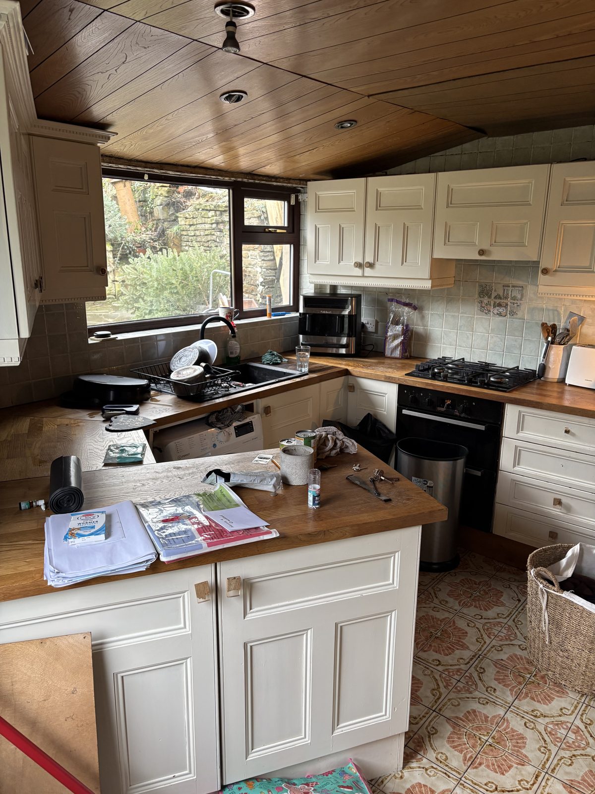 Kitchen before renovation, with cream raised-panel cabinets, oak worktops and a wood-panelled ceiling
